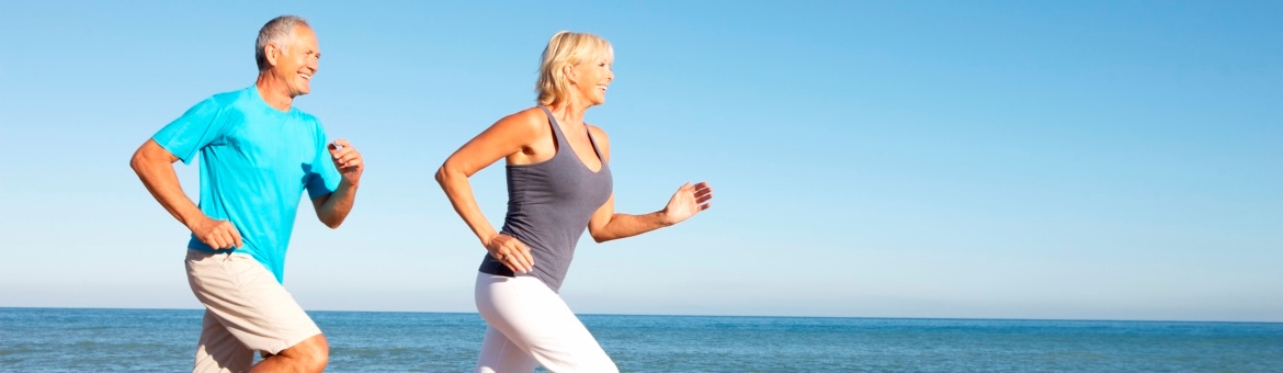 Senior Couple In Fitness Clothing Running Along Beach
